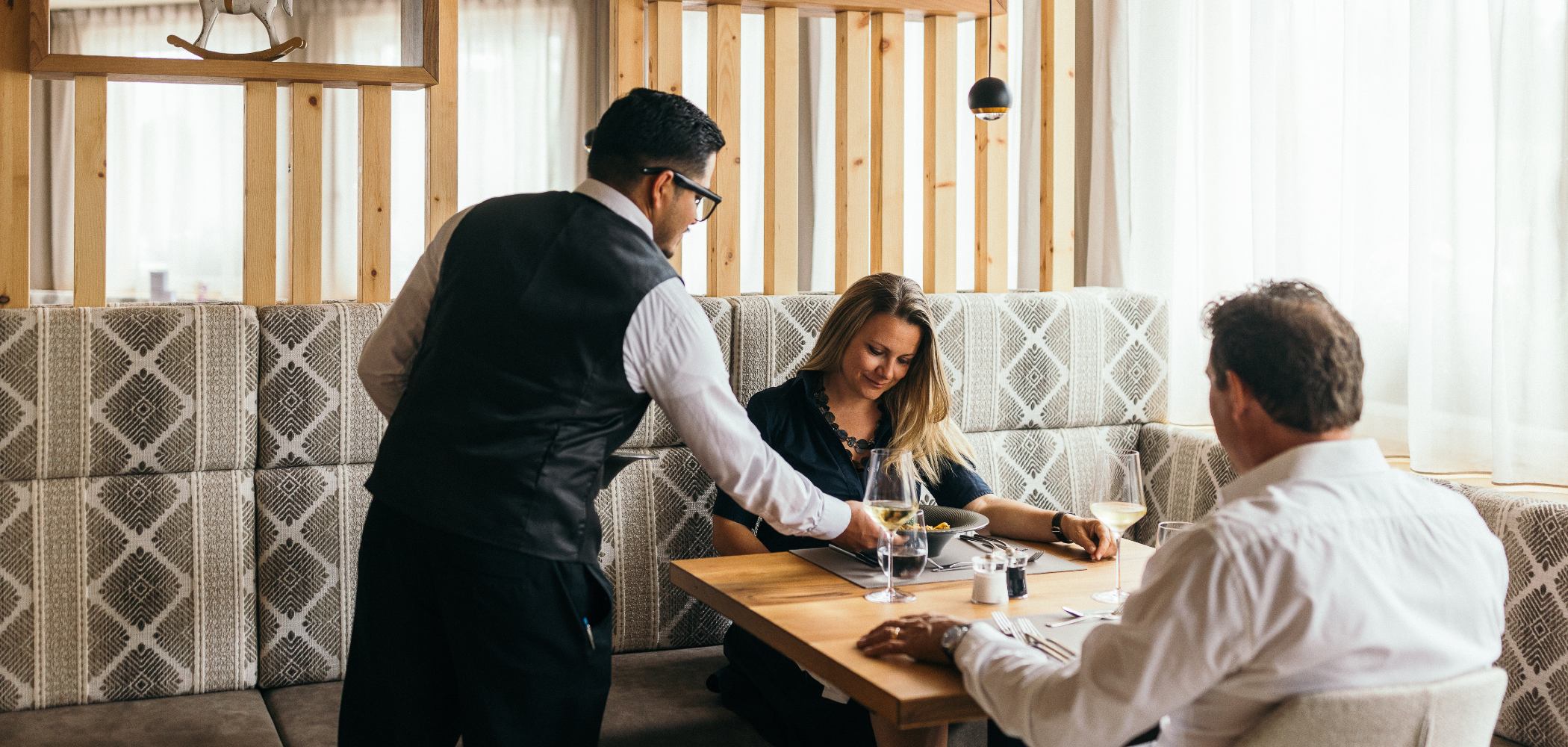 Zwei Erwachsene beim Abendessen und ein Kellner serviert