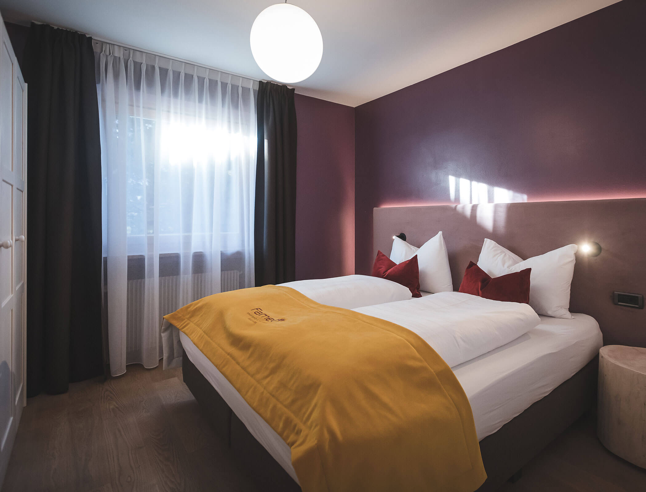Ein modernes Schlafzimmer mit zwei Betten, einer gelben Decke, burgunderroten Wänden, weißen Vorhängen und hereinströmendem Sonnenlicht. - Hotel Fameli