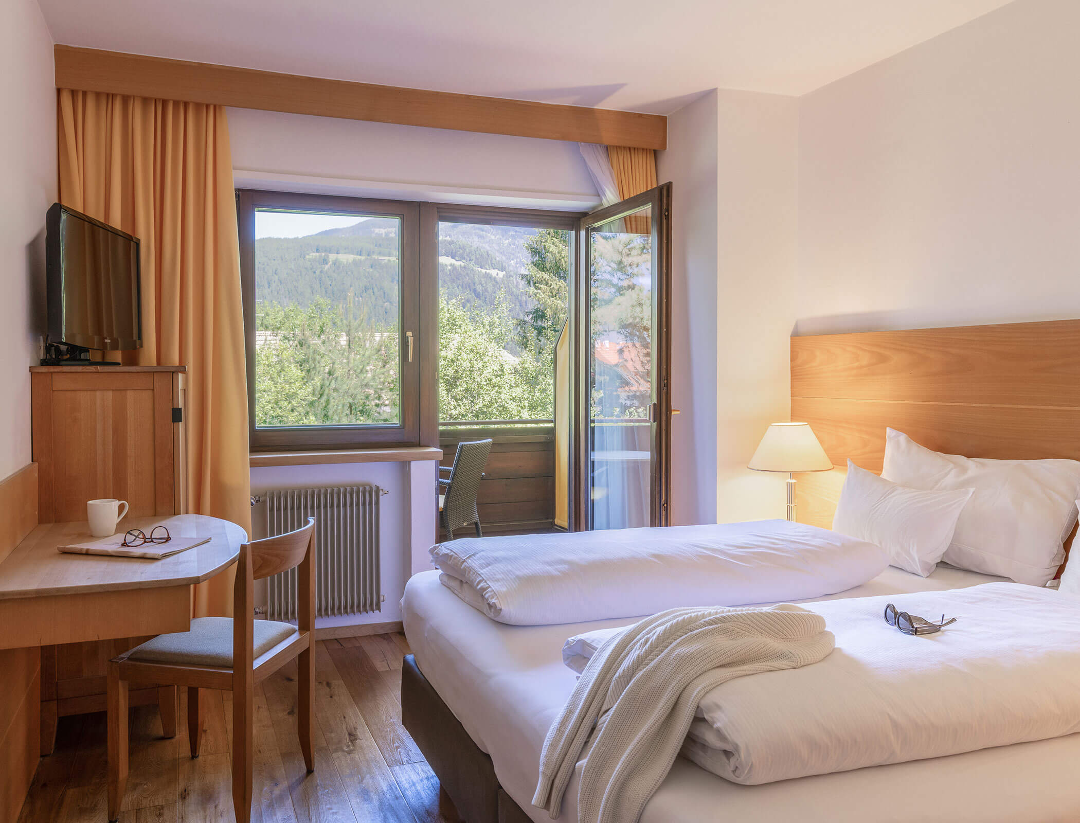 Cozy hotel room with double bed, desk, TV, open window, and scenic mountain view outside. - Hotel Fameli
