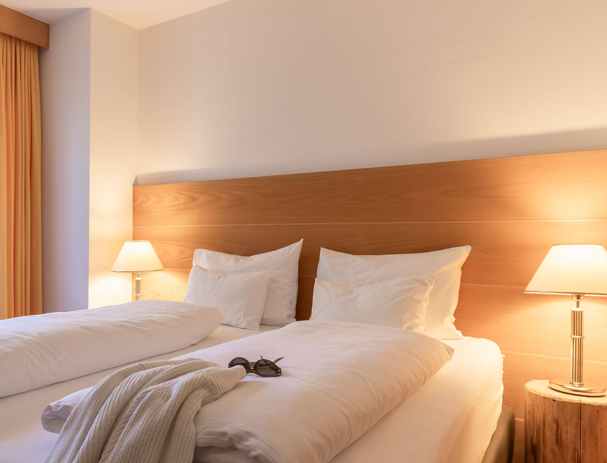 Two twin beds with white bedding, bedside lamps, and a folded sweater with sunglasses on the bed. - Hotel Fameli