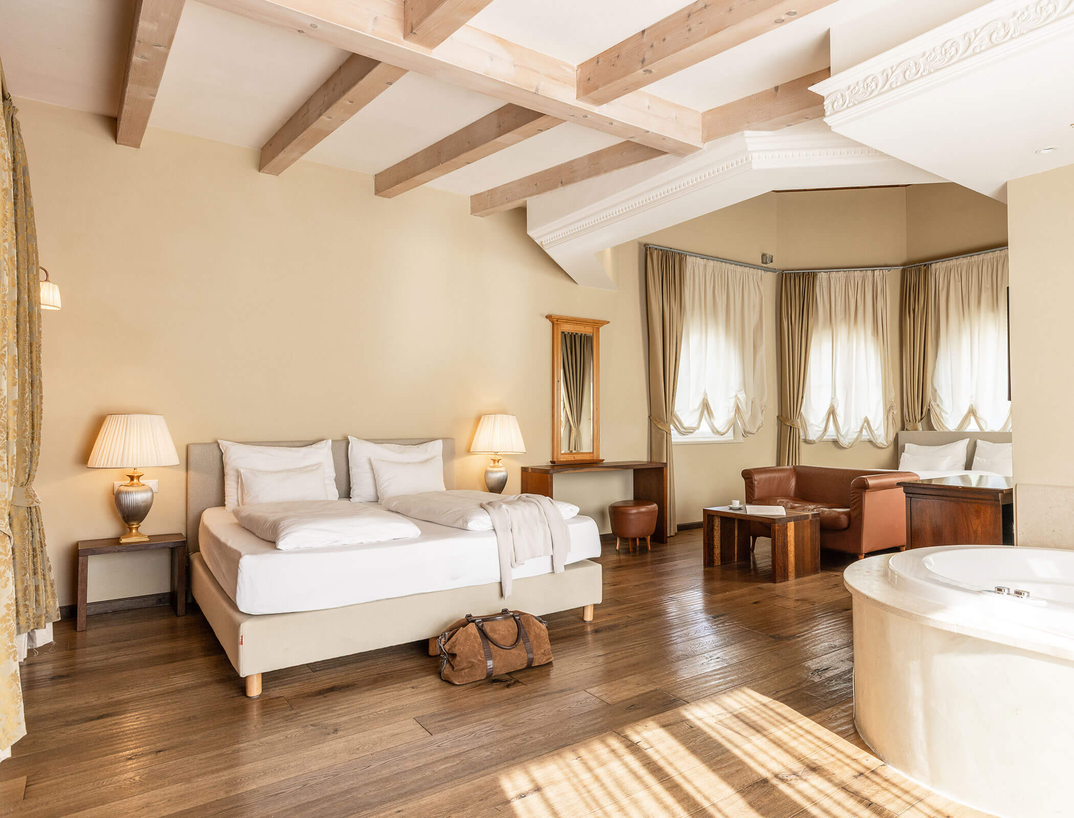 Elegant hotel suite with a large bed, seating area, and a jacuzzi tub in a bright, spacious room. - Hotel Fameli
