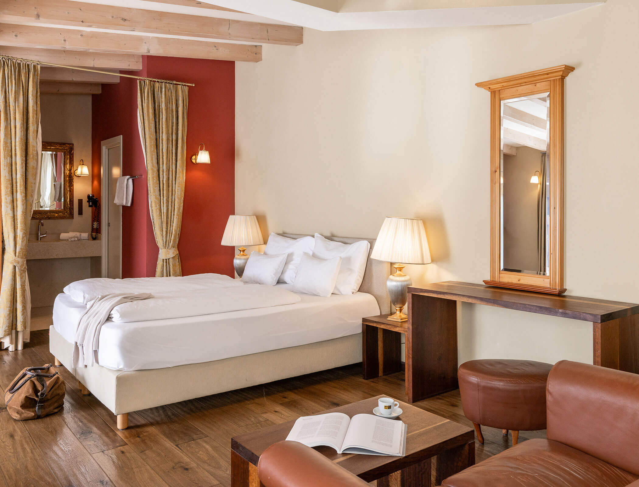 Hotel room with a bed, lamps, mirror, armchairs, coffee table, open book, and an open bag on the floor. - Hotel Fameli