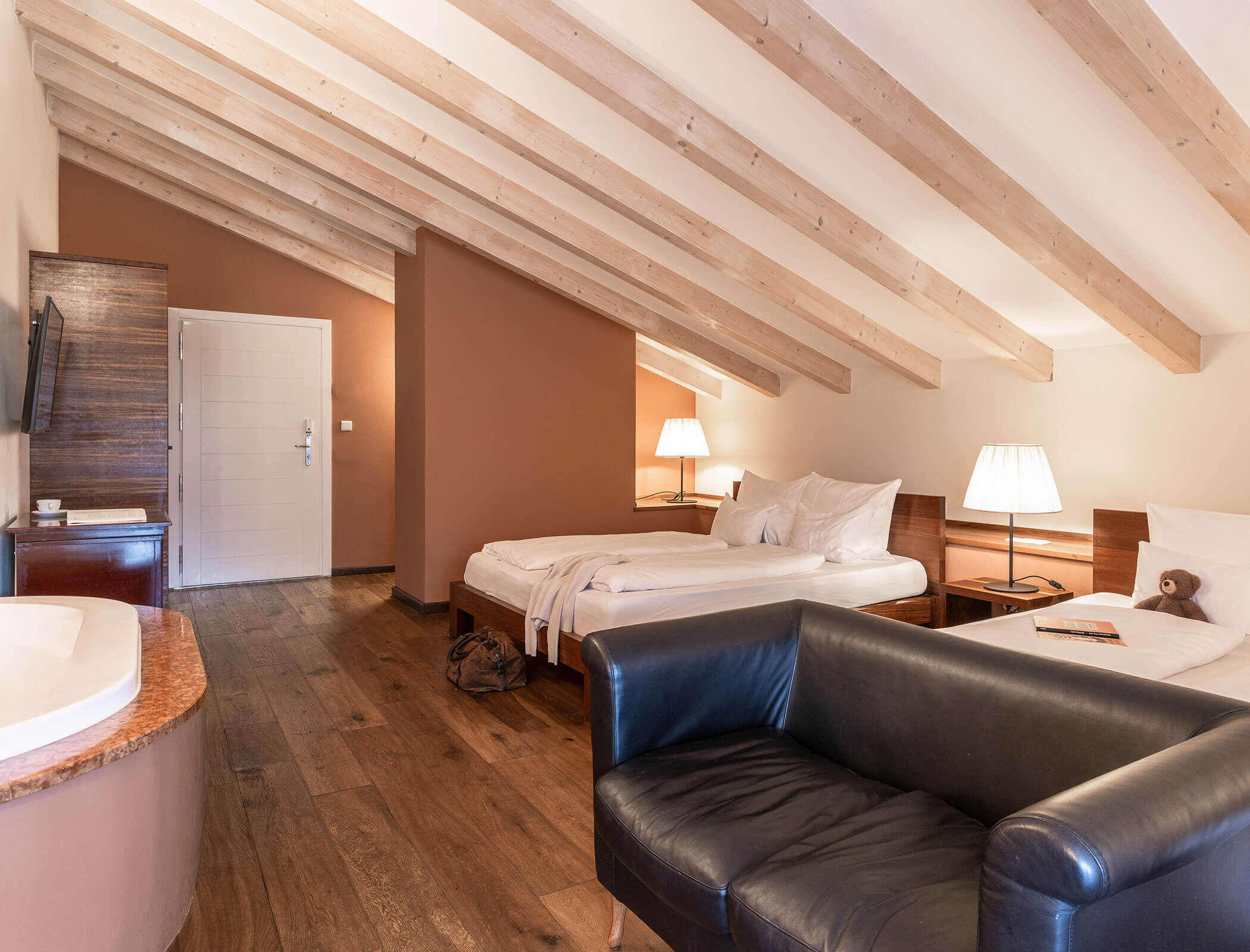 Hotel room with two beds, a black sofa, wooden beams, lamps, and a small table on a wooden floor. - Hotel Fameli