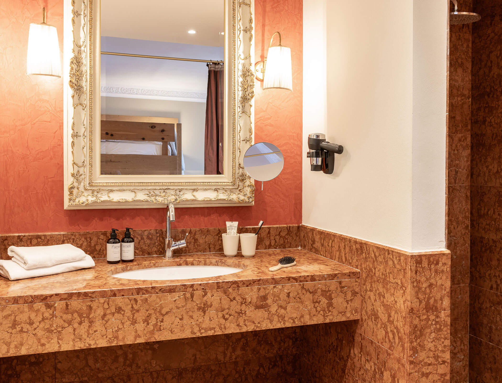 Elegant bathroom with a marble countertop, sink, mirror, towels, toiletries, and warm lighting. - Hotel Fameli