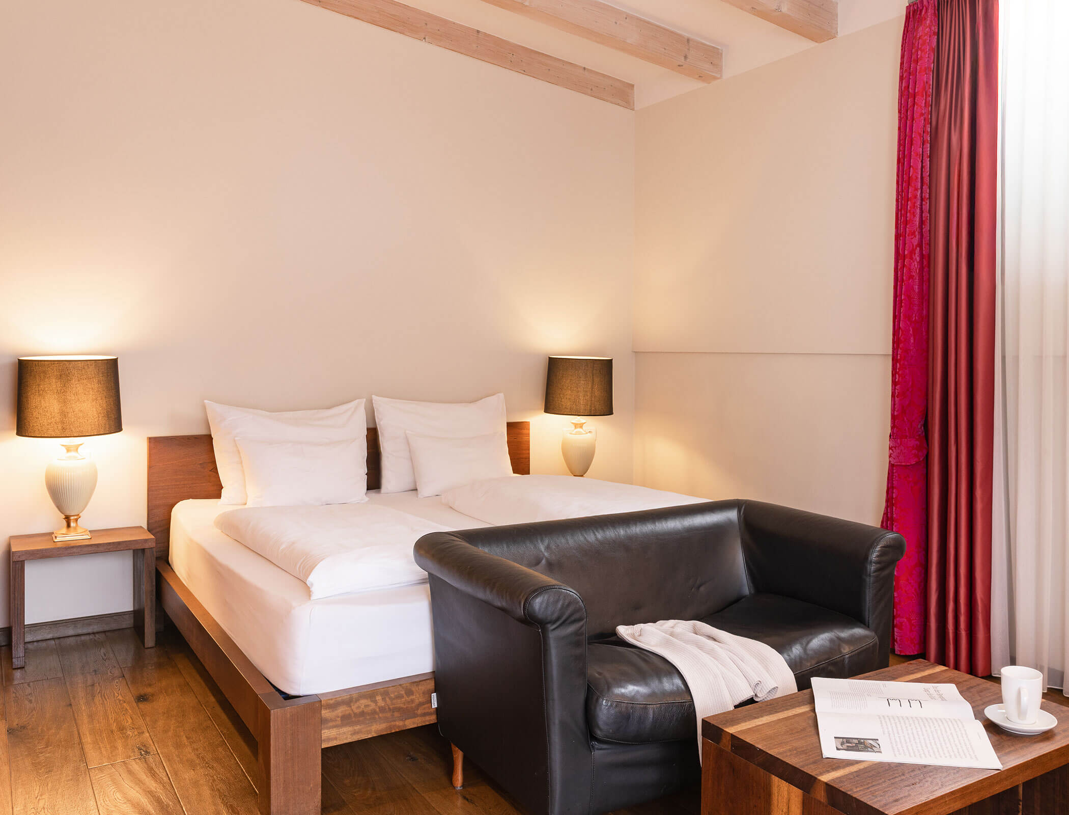A cozy hotel room with a double bed, black sofa, wooden tables, and two lamps by the bedside. - Hotel Fameli
