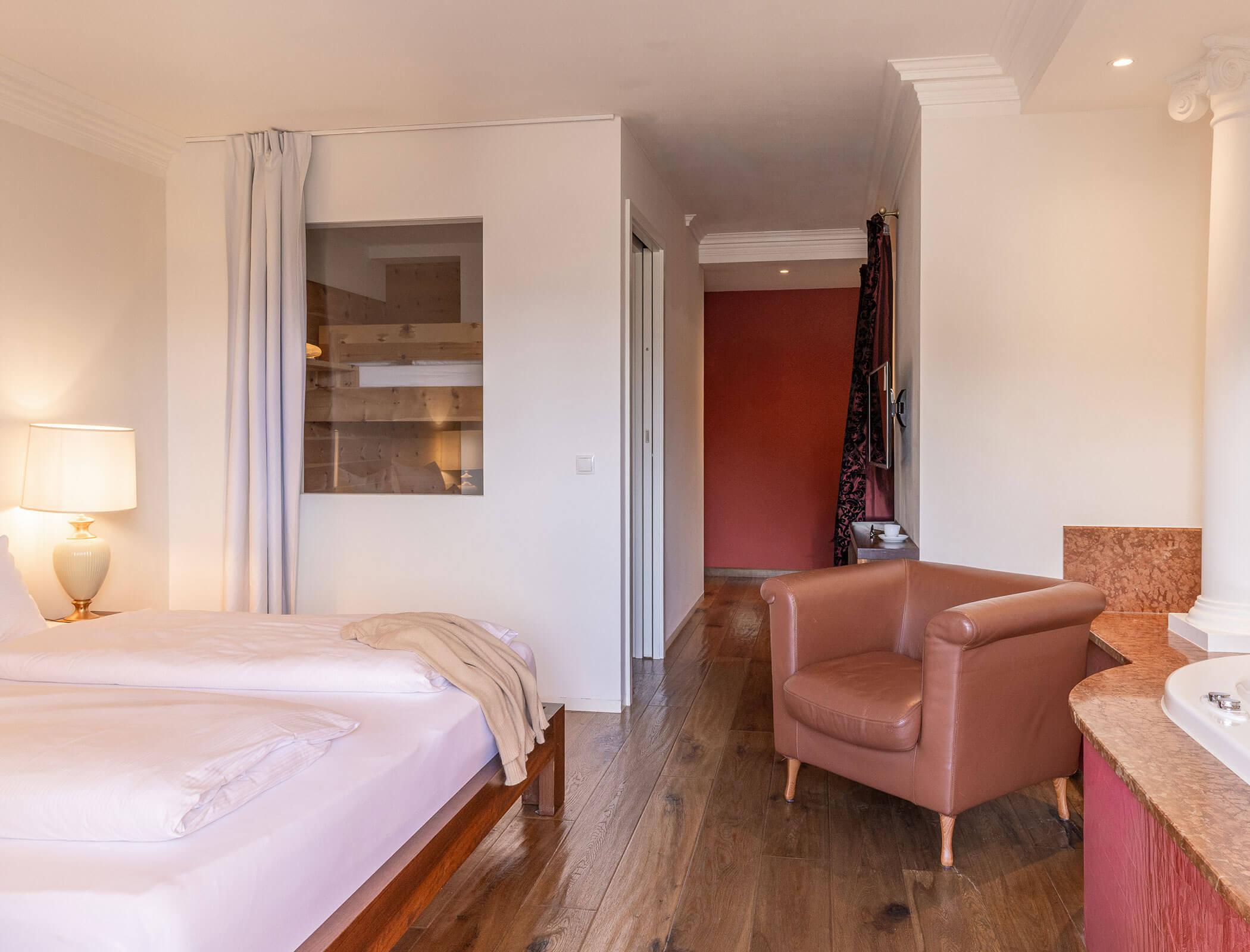 A hotel room with a double bed, armchair, lamp, window, and wooden floor. - Hotel Fameli