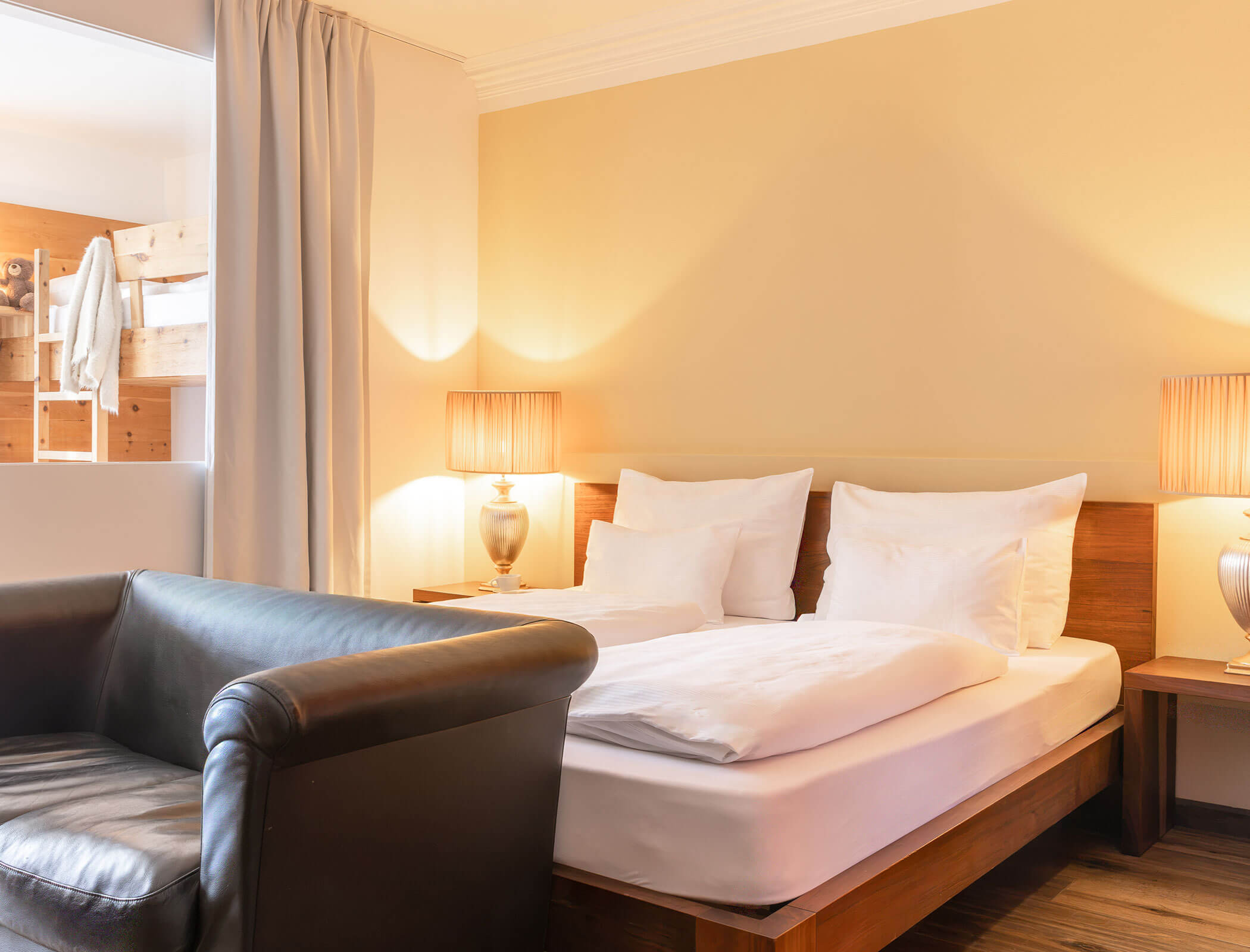 A cozy hotel room with a double bed, two lamps, a leather sofa, and warm lighting. - Hotel Fameli