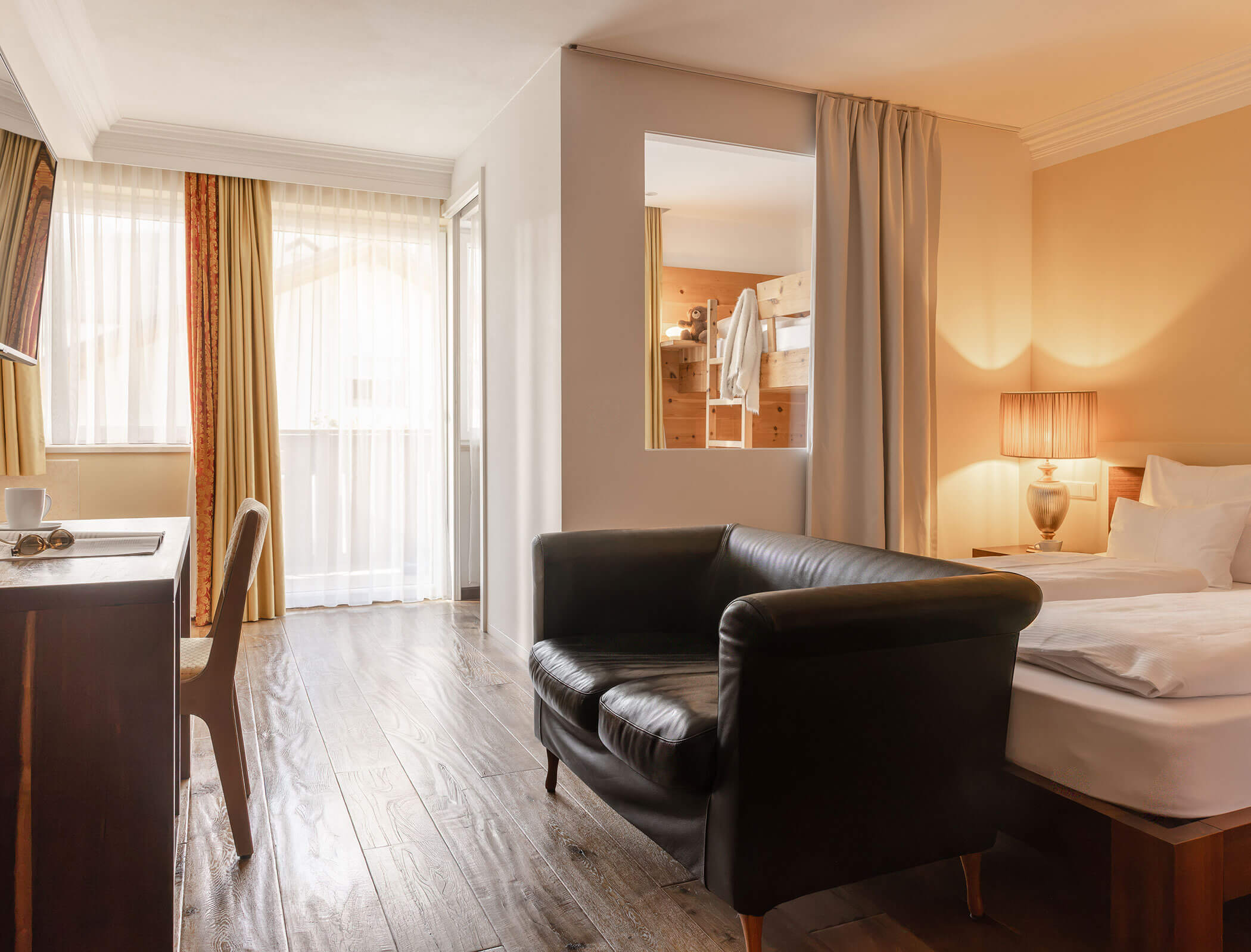 Hotel room with a black armchair, bed, desk, large window, and a bunk bed in an adjacent area. - Hotel Fameli
