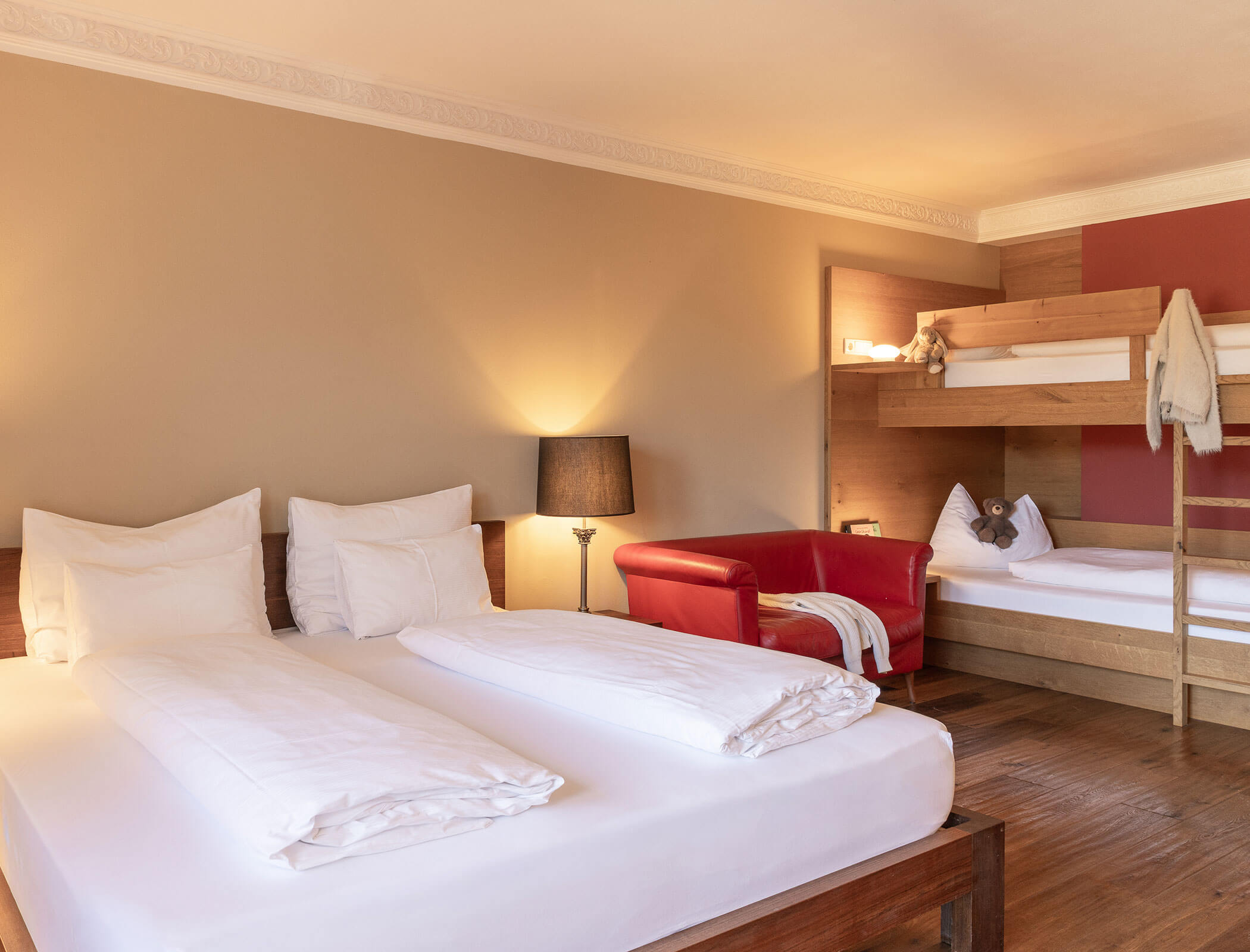 Hotel room with a double bed, bunk beds, red armchair, lamp, and wooden floor. - Hotel Fameli