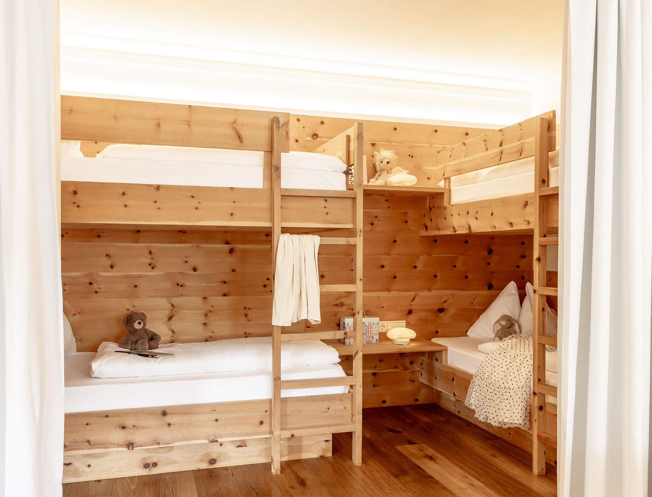 Four wooden bunk beds with white bedding, toys, and stuffed animals in a cozy, wood-paneled room. - Hotel Fameli