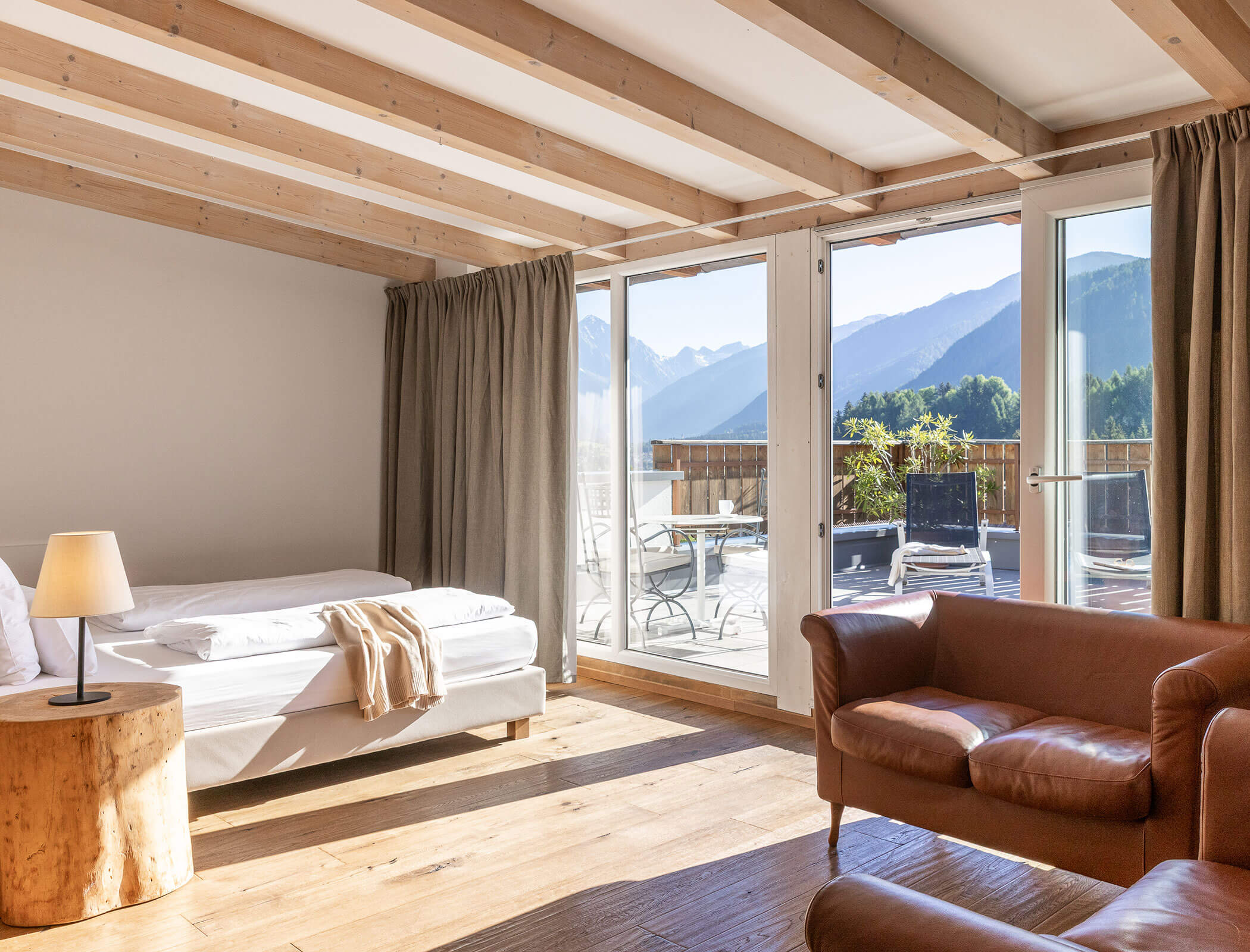Bright room with a bed, brown armchair, wood accents, and mountain view through large glass doors. - Hotel Fameli