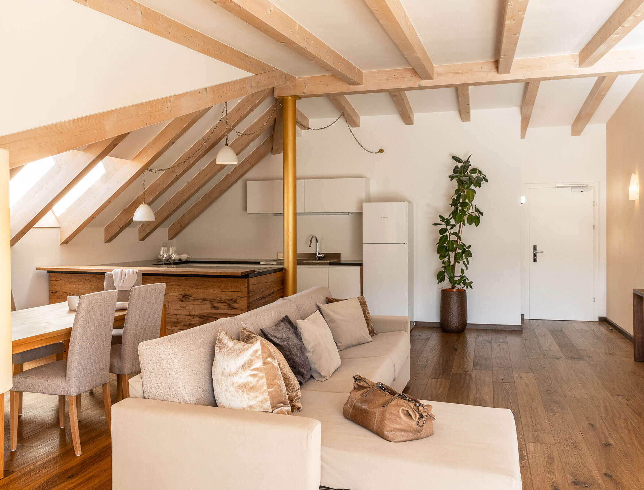 Modern loft with wooden beams, kitchen, dining area, beige sofa, and potted plant near the white door. - Hotel Fameli
