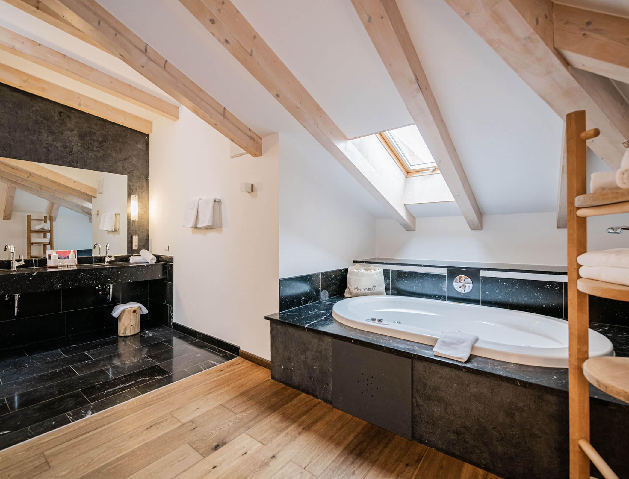 Modern attic bathroom with a skylight, bathtub, double sinks, and wooden beams on the slanted ceiling. - Hotel Fameli